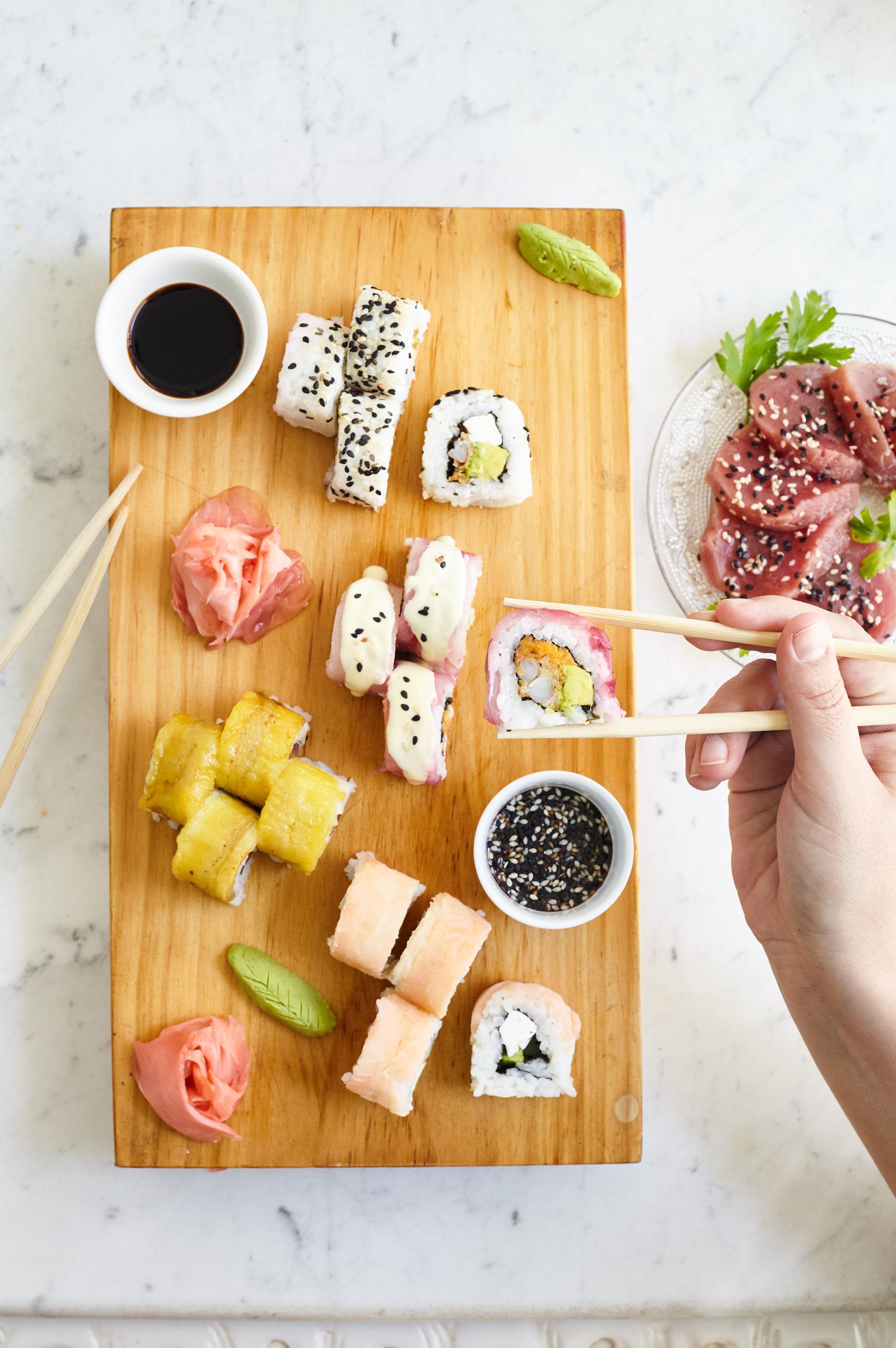 A person is eating sushi with chopsticks on a wooden cutting board.