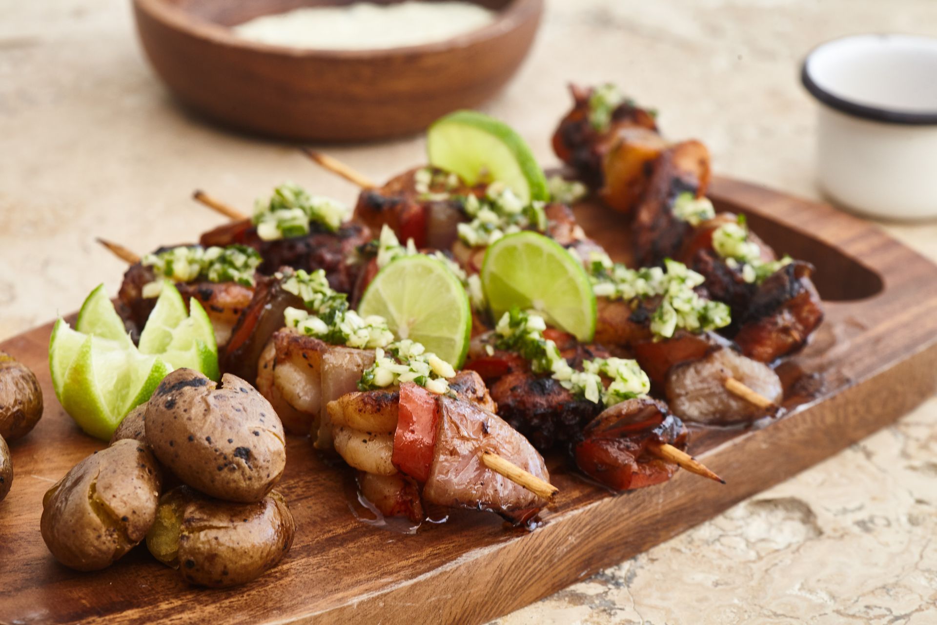 A wooden cutting board topped with skewers of meat and potatoes.