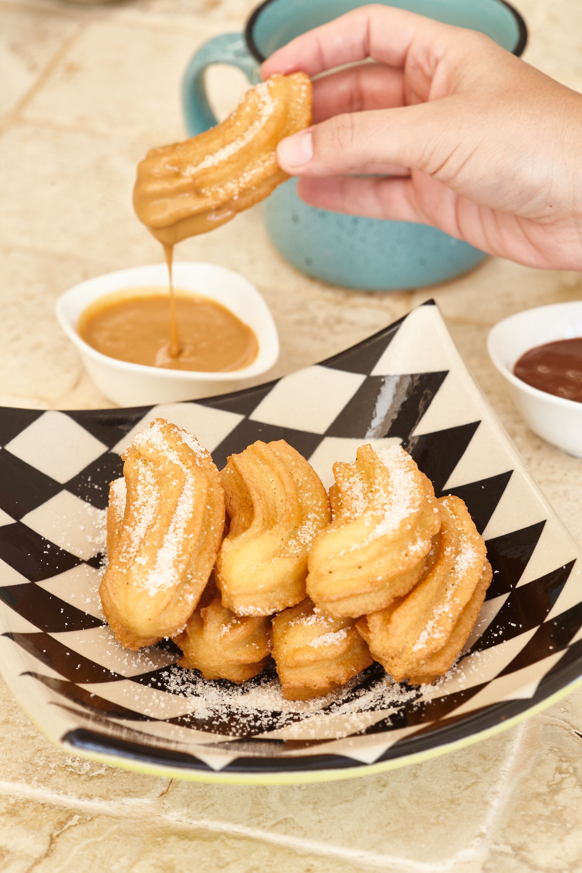 A person is dipping churros in chocolate sauce on a plate.