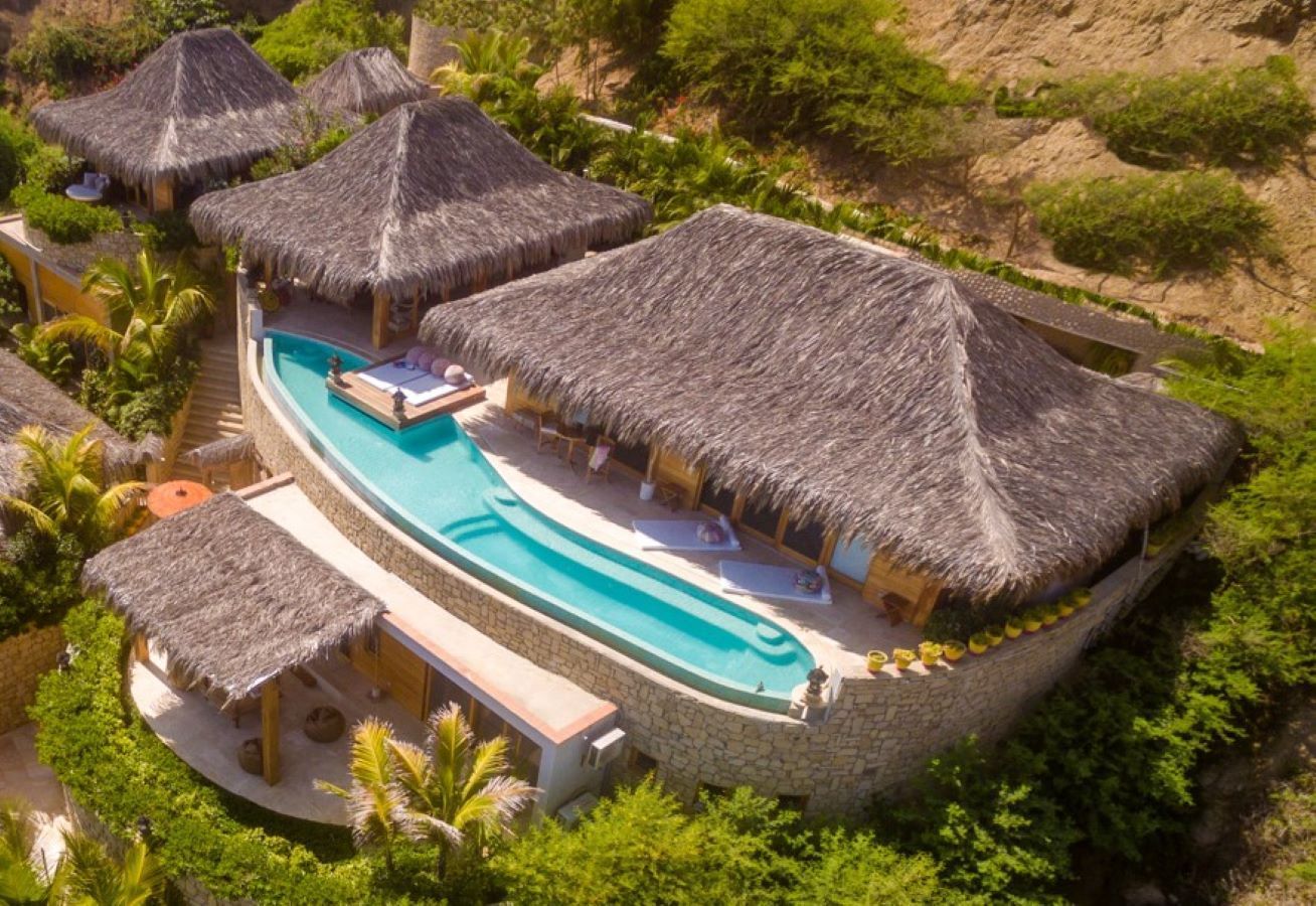 An aerial view of a tropical resort with thatched roofs and a swimming pool.
