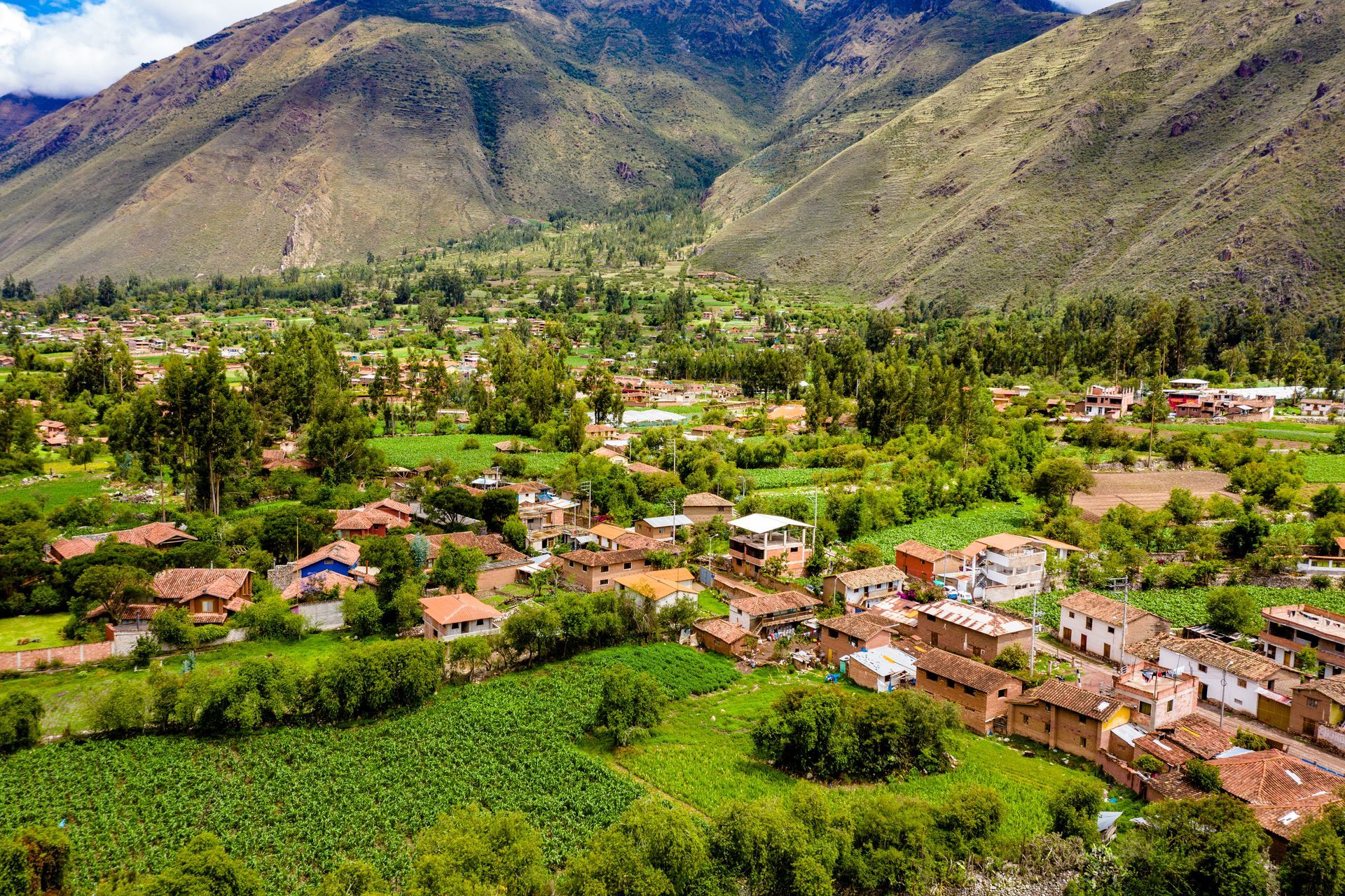 An aerial view of a small village in the middle of a lush green valley surrounded by mountains.