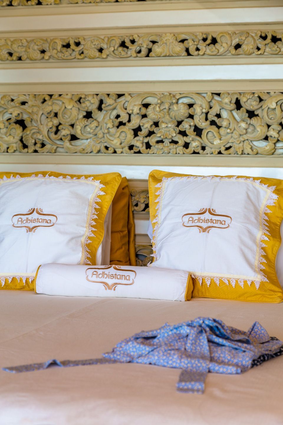 A bed with yellow and white pillows and a blue tie on it.