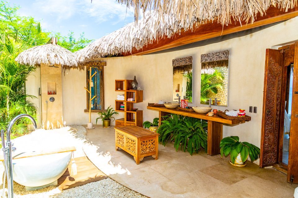 A bathroom with a bathtub , sinks , mirrors and a thatched roof.