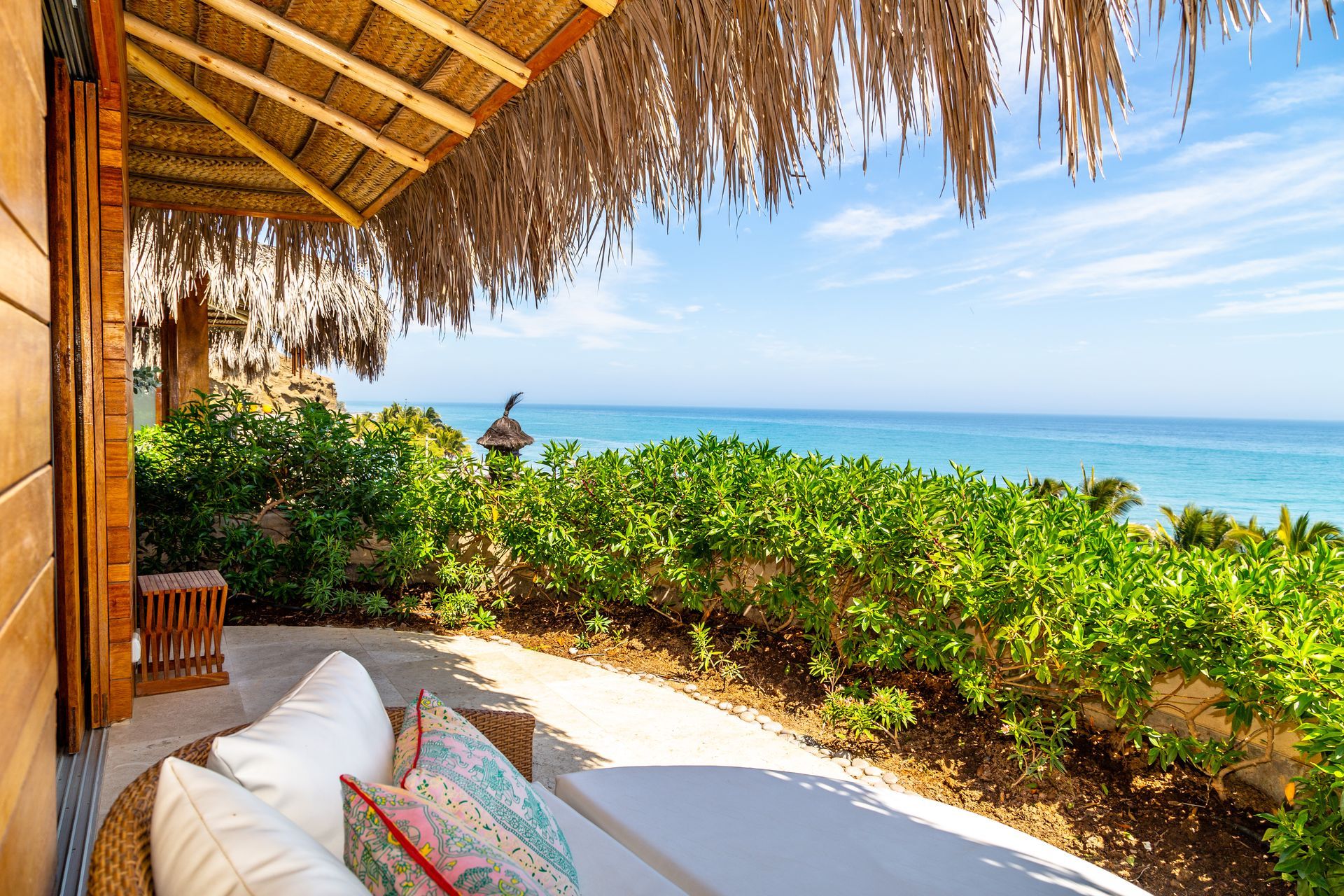 A patio with a thatched roof overlooking the ocean.