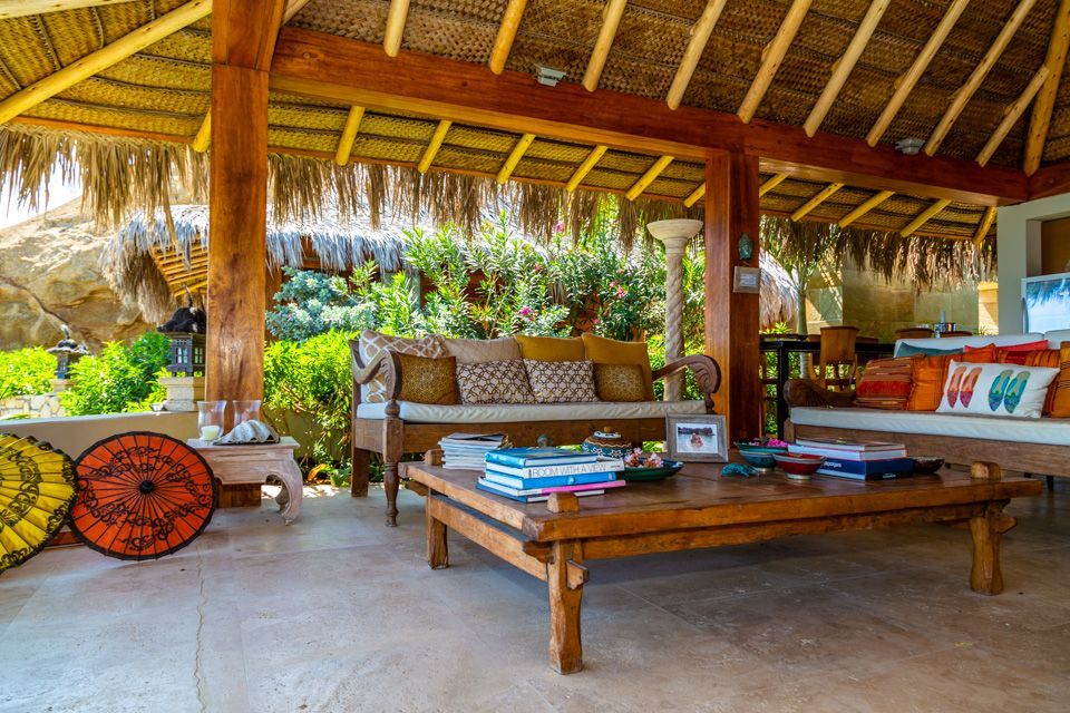 A living room with a couch , table and umbrellas under a thatched roof.