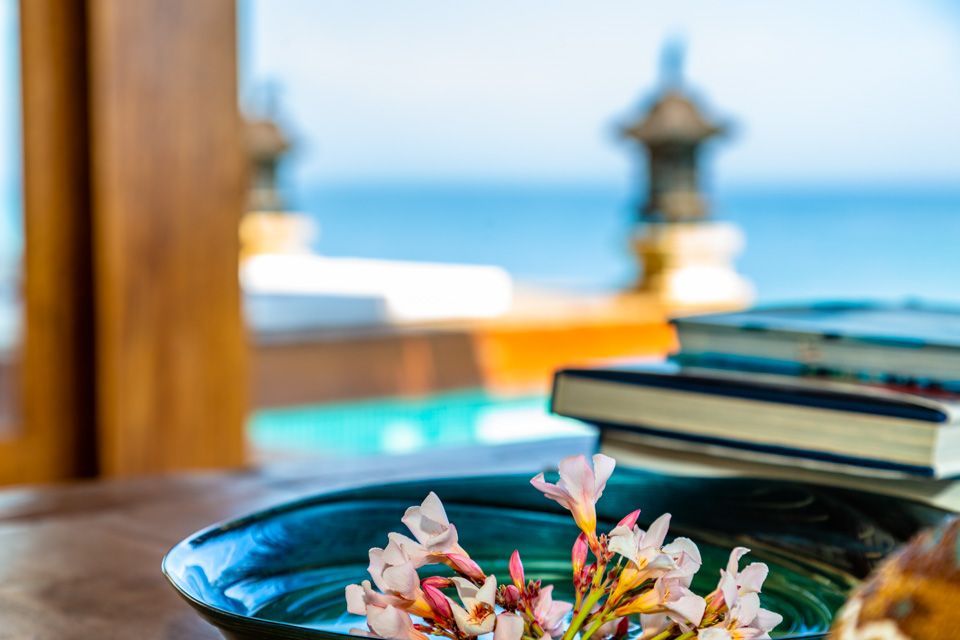 A bowl of flowers is sitting on a table next to a stack of books.