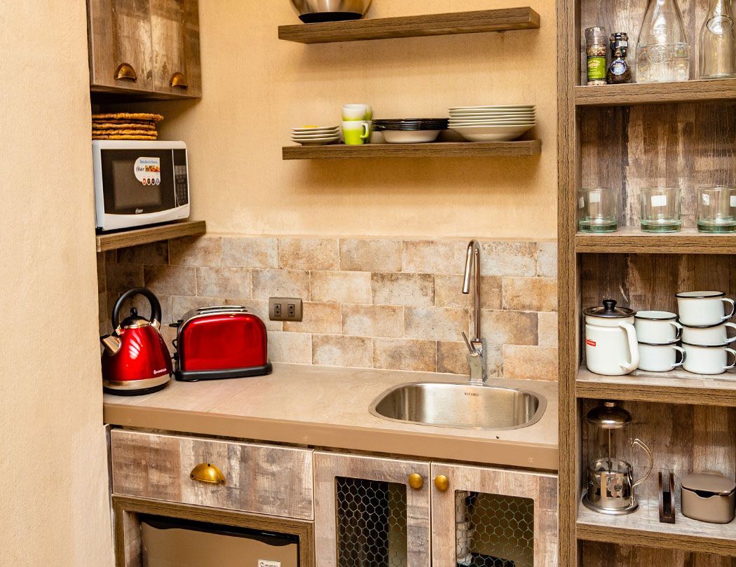 A kitchen with a sink , microwave , toaster oven , and shelves.