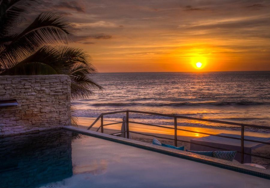 A sunset over the ocean with a swimming pool in the foreground.