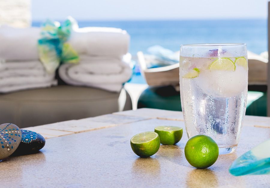 A glass of water with ice and limes on a table.
