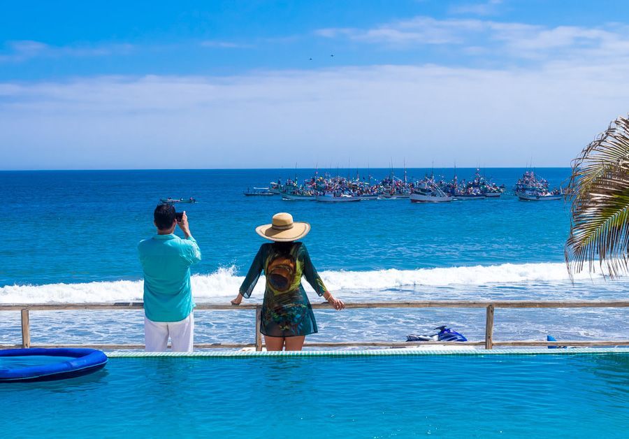 A man and a woman are standing next to a swimming pool overlooking the ocean.