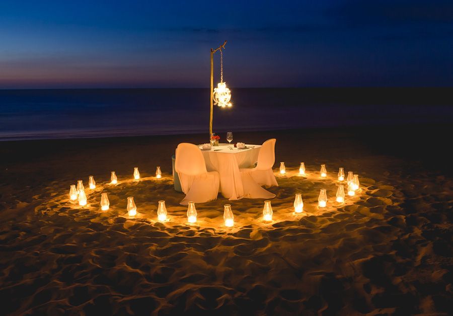 There is a table and chairs on the beach with candles around it.