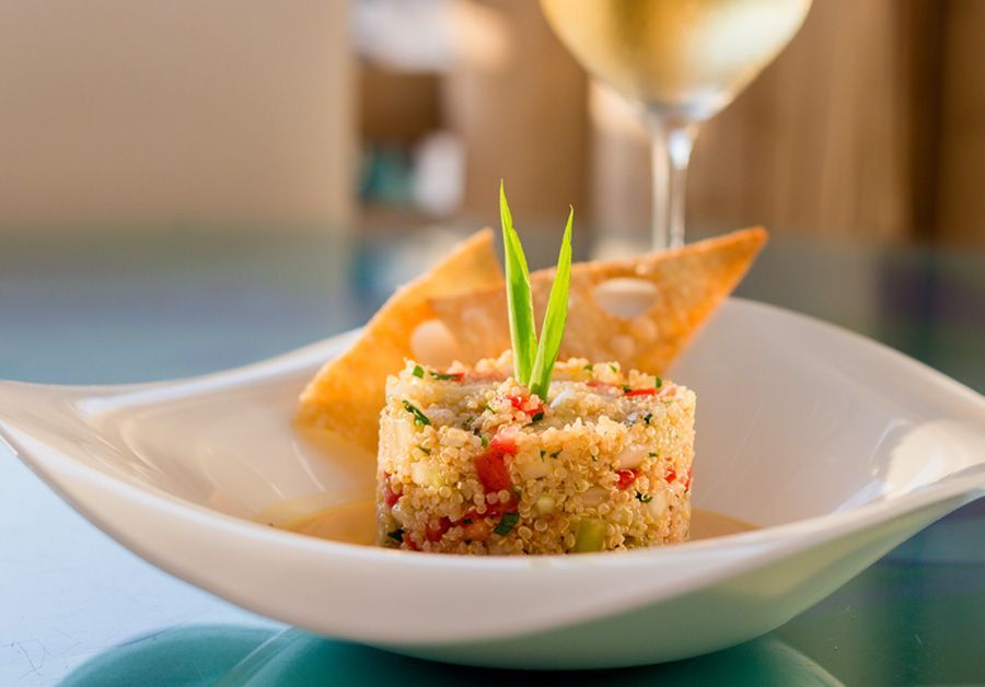A close up of a plate of food with a glass of wine in the background.