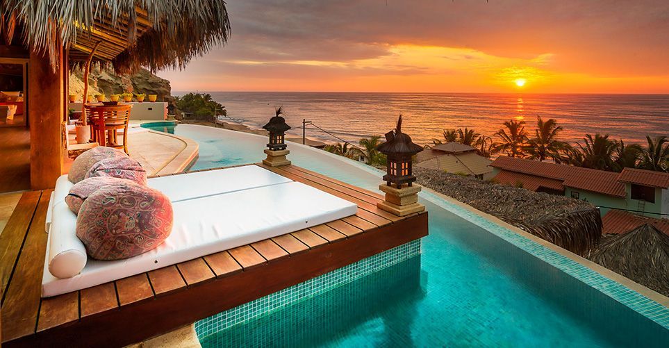 There is a swimming pool with a view of the ocean at sunset.