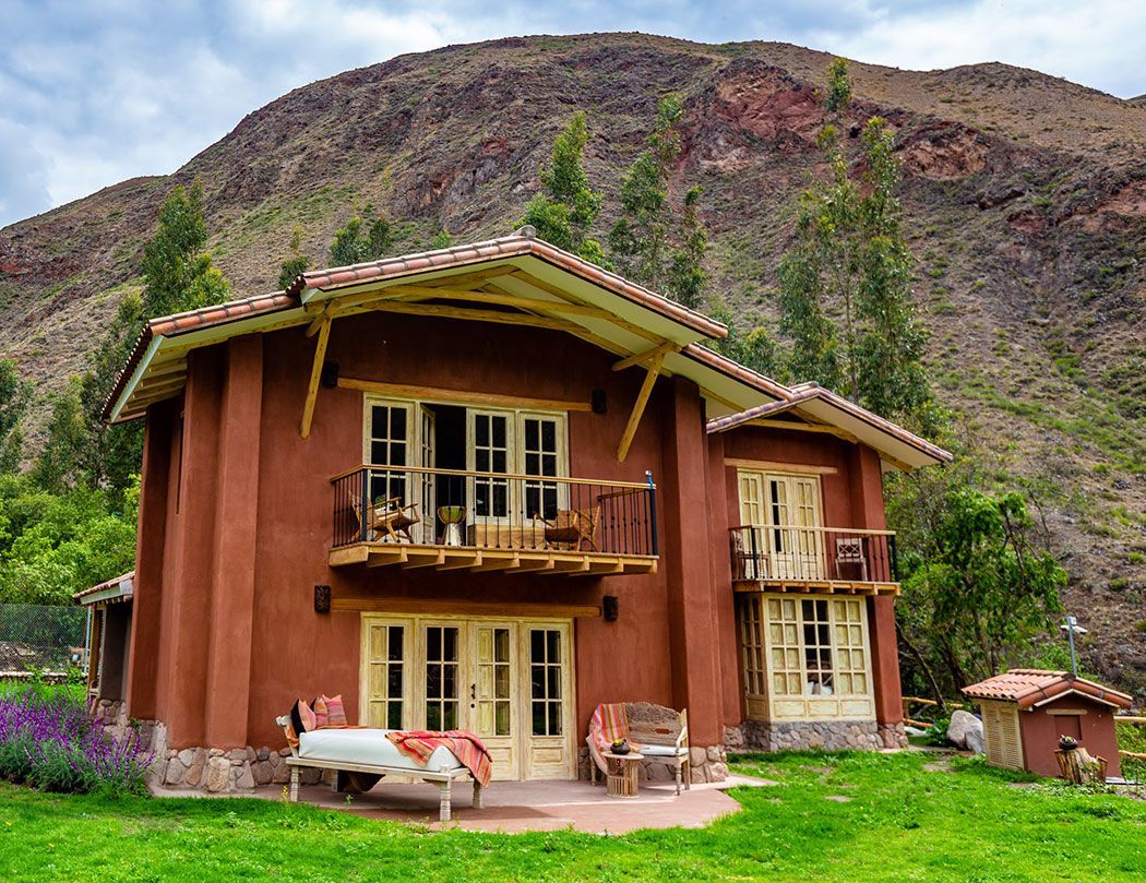 A large house with a mountain in the background is sitting in the middle of a lush green field.