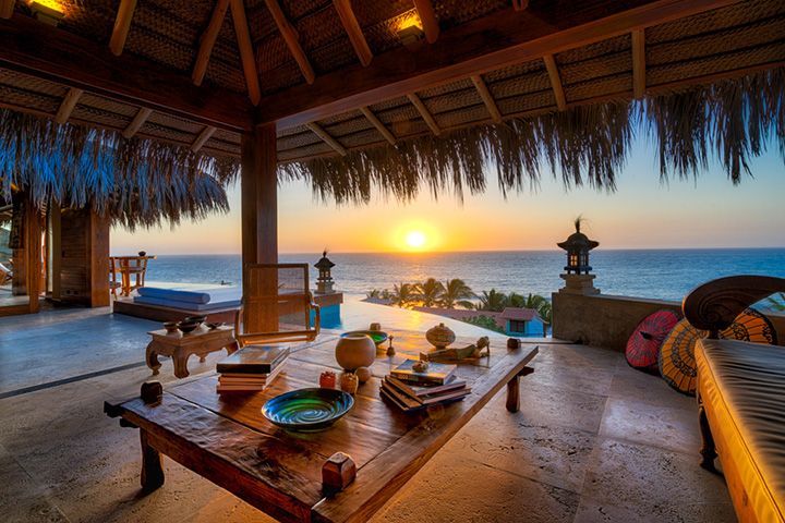 A living room with a table and a view of the ocean at sunset.