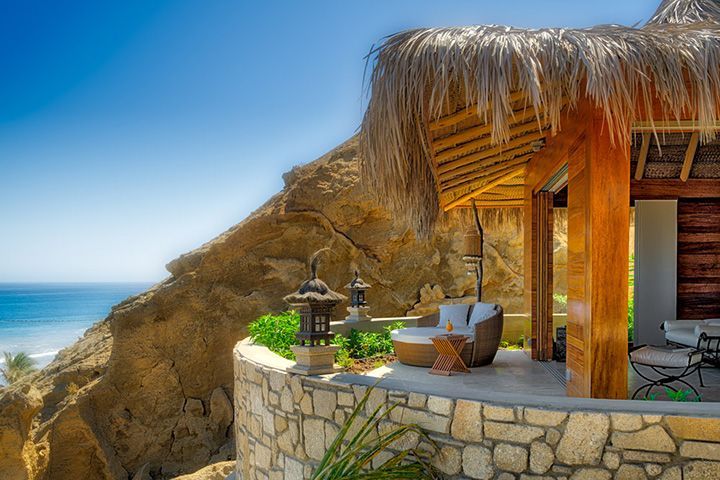 A house with a thatched roof sits on top of a cliff overlooking the ocean.