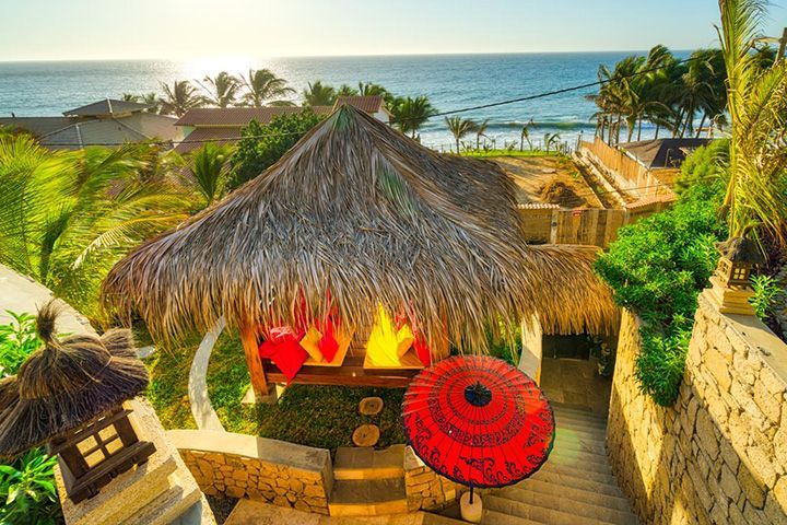 A thatched hut with two red umbrellas in front of the ocean.