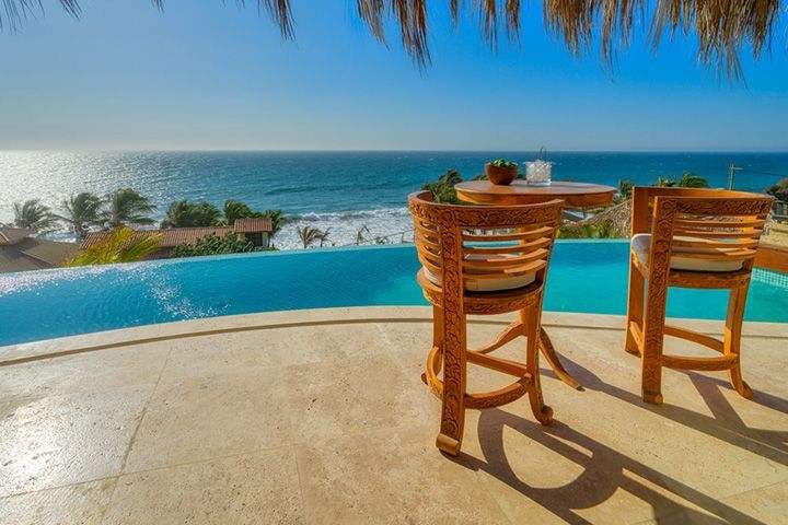 Two chairs are sitting next to a swimming pool overlooking the ocean.