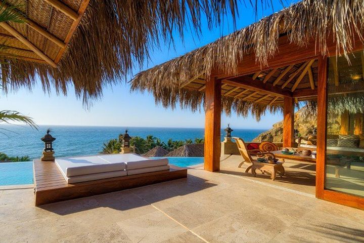 A house with a thatched roof and a swimming pool overlooking the ocean.