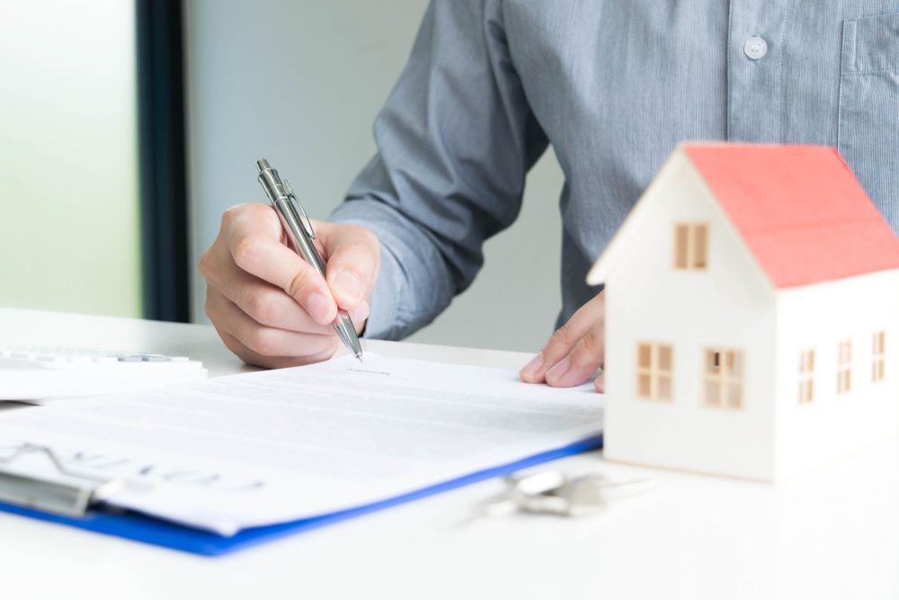 Person Signing Documents Next to a Miniature House — Midcoast Financial Planning Group in Forster, NSW