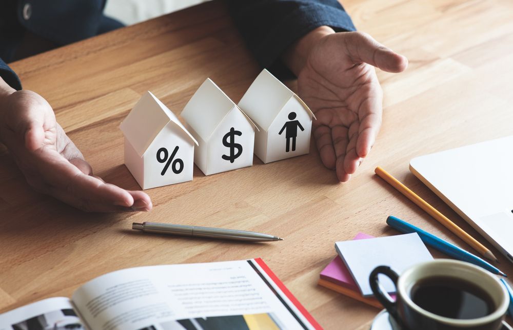 Hands Protecting Paper Houses With Percentage, Dollar Sign — Midcoast Financial Planning Group in Forster, NSW