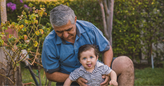 Man Holding A Baby With A Playful Expression — Midcoast Financial Planning Group in Tuncurry, NSW