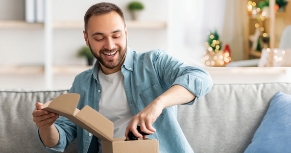 Man on Couch, Smiling as He Opens a Cardboard Box. Living Room Setting — Midcoast Financial Planning Group in Tuncurry, NSW