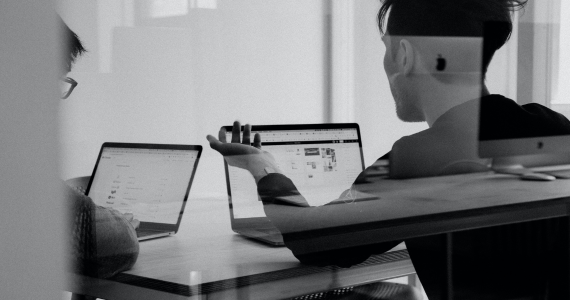 Two People At A Desk With Laptops, One Gestures Toward A Screen. Office Setting — Midcoast Financial Planning Group in Tuncurry, NSW