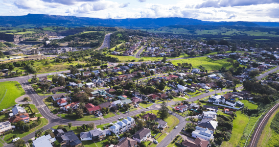 Aerial View Of A Suburban Community With Houses, Roads, And Green Spaces, Under A Cloudy Sky With Mountains In The Background — Midcoast Financial Planning Group in Tuncurry, NSW