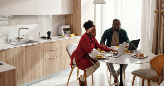 Couple Working On Laptops At A Kitchen Table — Midcoast Financial Planning Group in Tuncurry, NSW