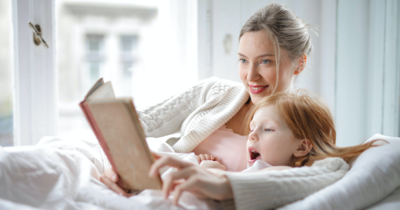 Woman Reads A Book With A Child In Bed — Midcoast Financial Planning Group in Tuncurry, NSW