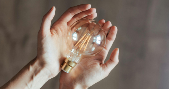 Hands Cupped, Holding a Clear Lightbulb — Midcoast Financial Planning Group in Tuncurry, NSW