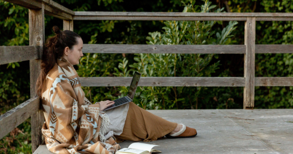 Woman Works On Laptop, Sitting On A Wooden Deck — Midcoast Financial Planning Group in Tuncurry, NSW