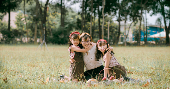 Woman Kneels in A Grassy Field, Hugging Two Children — Midcoast Financial Planning Group in Tuncurry, NSW