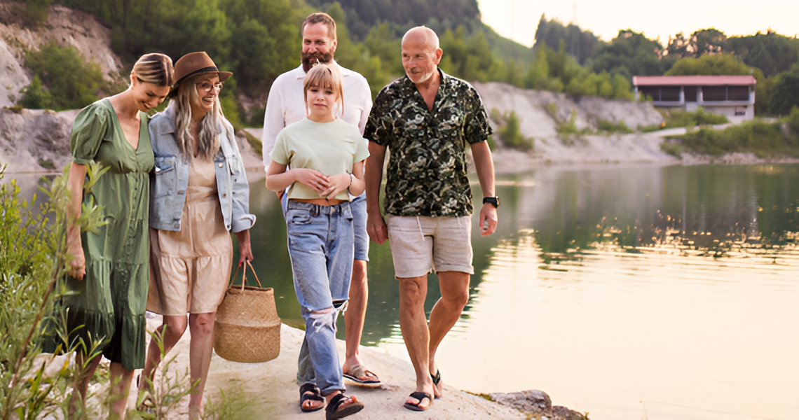 Group of people walking near a lake: shoreline, dressed in summer clothes, sunny day.