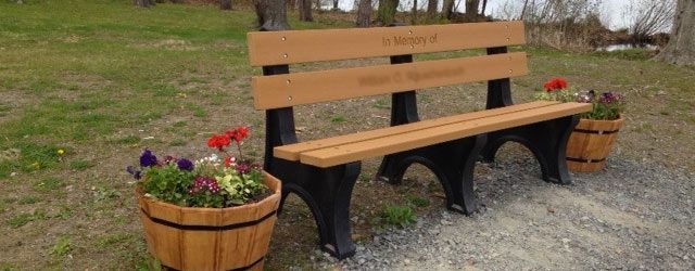 A wooden park bench with two buckets of flowers next to it.