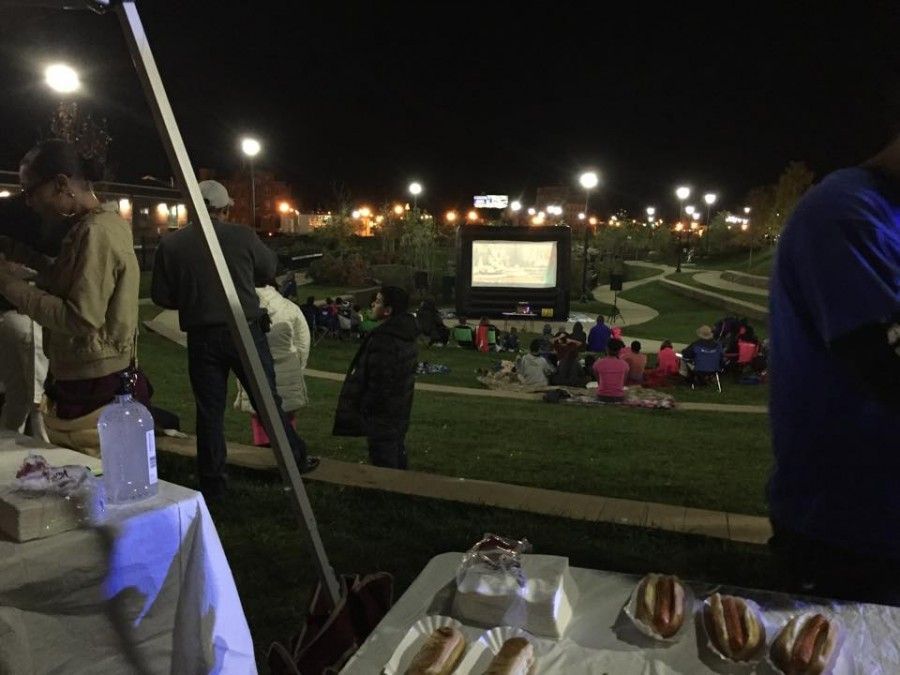 A group of people are watching a movie in a park at night.