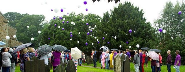 A group of people are standing in a field with balloons flying in the air.