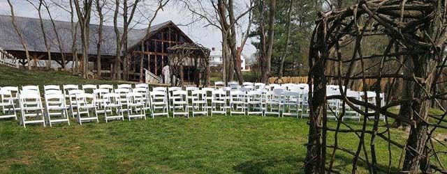 A row of white chairs are lined up in front of a barn.