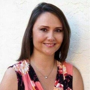 A woman wearing a floral top and a necklace is smiling for the camera.