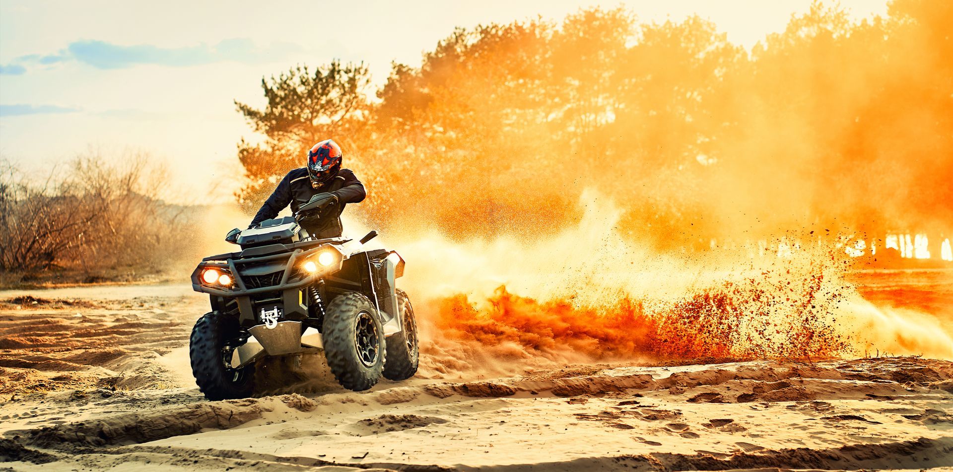 ATV racing through dirt with a rider amid a large orange dust cloud