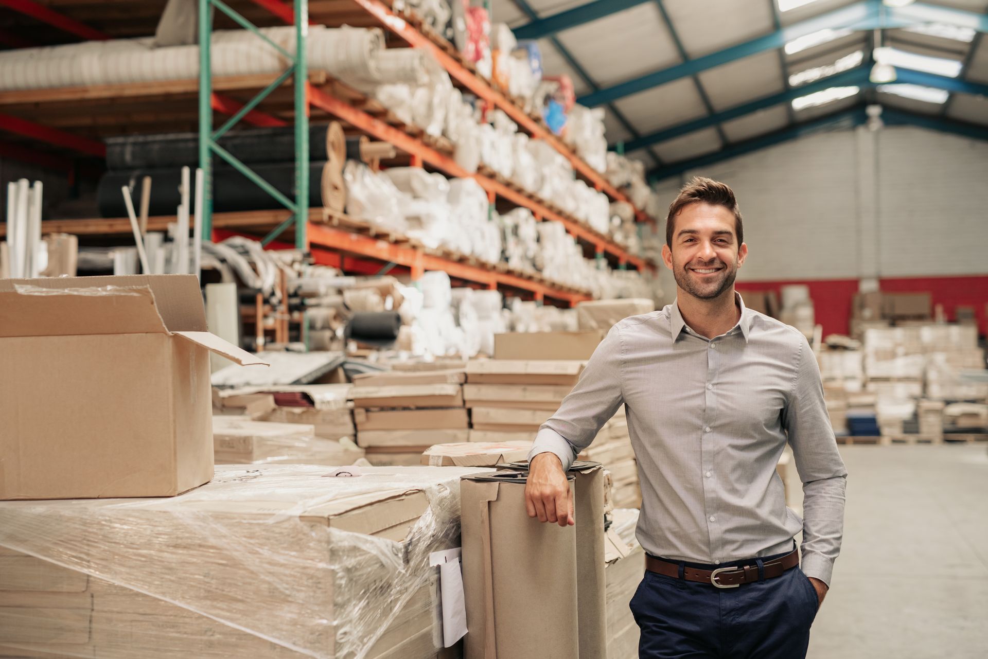 A professional standing and smiling in a warehouse filled with shelves of fabric rolls and stacked boxes.