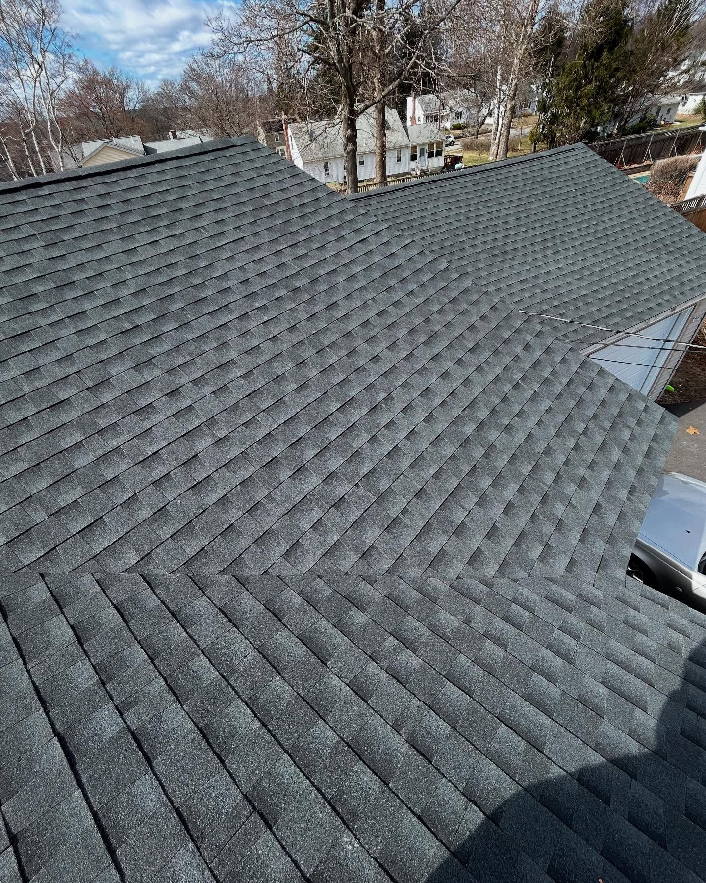 Dark gray asphalt shingle roof on a house, angled view, sunny day.