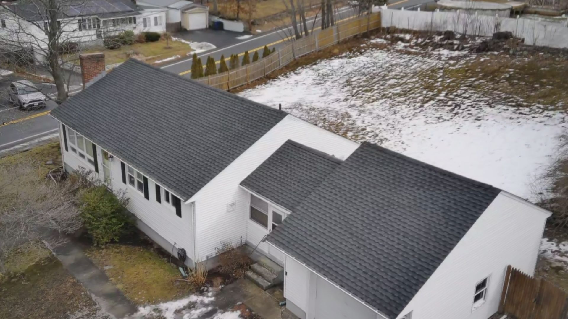 Aerial view of a white house with a dark gray roof, snow on the ground, and a street in front.