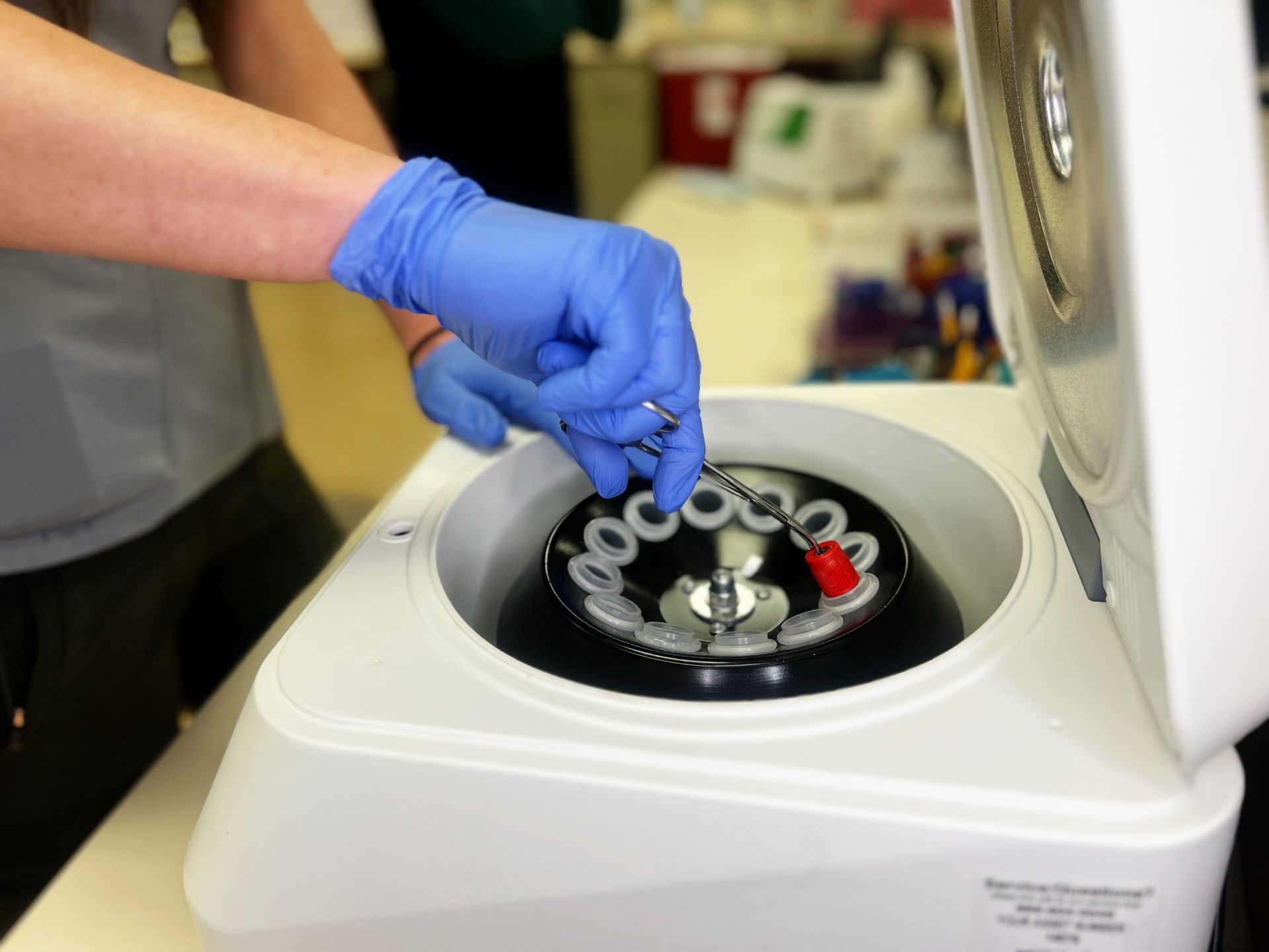 A person wearing blue gloves is putting something in a centrifuge | Intrepid Research