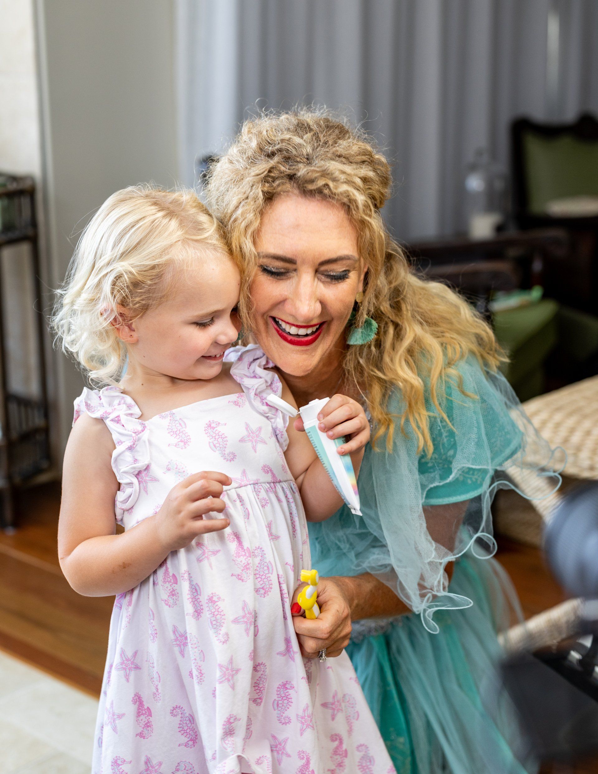 A woman and a little girl are brushing their teeth in front of a mirror.