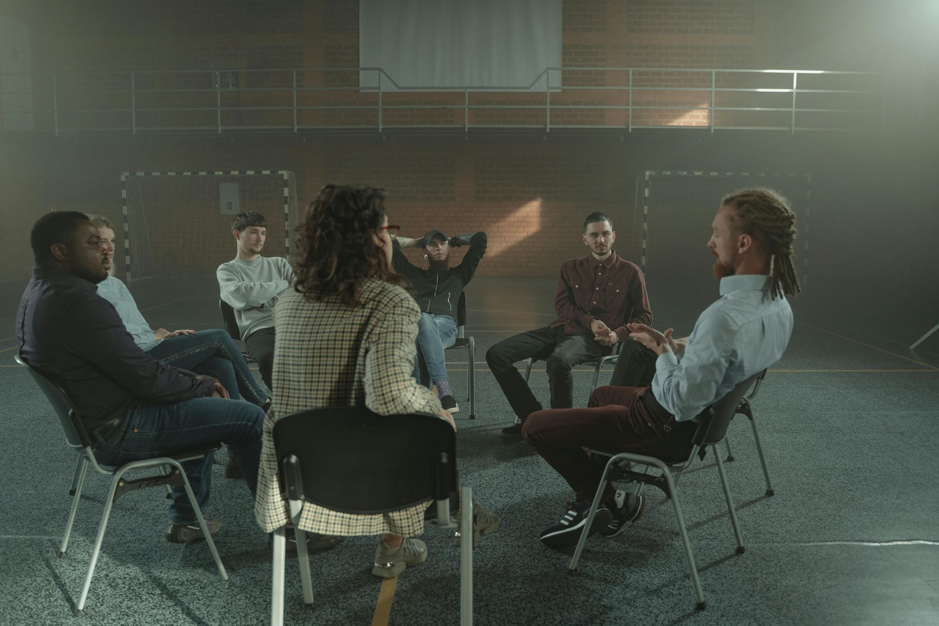A group of people are sitting in chairs in a circle having a conversation.