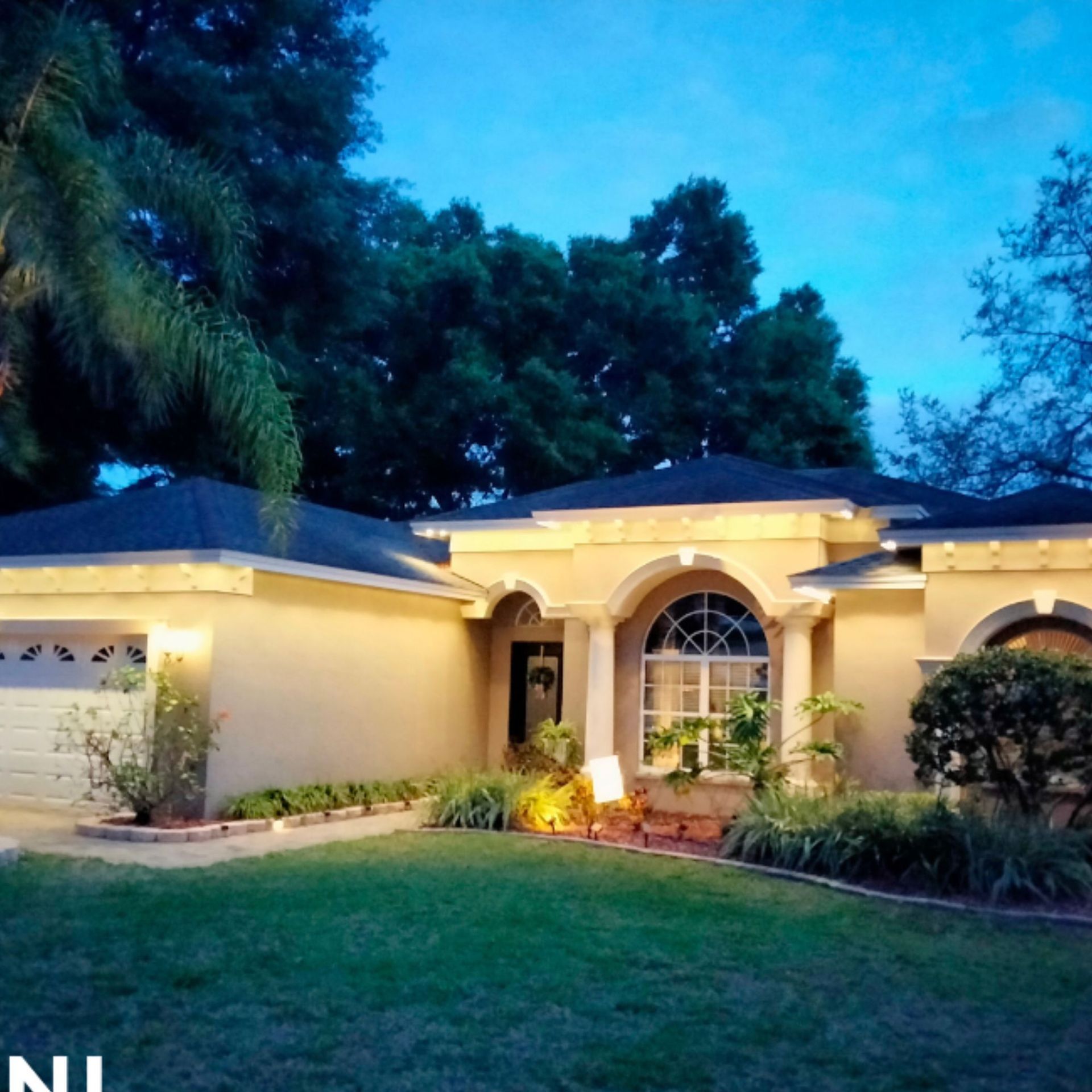 Silvers, Inc. - Beige house at dusk, arched entry with columns, and green lawn, surrounded by trees.