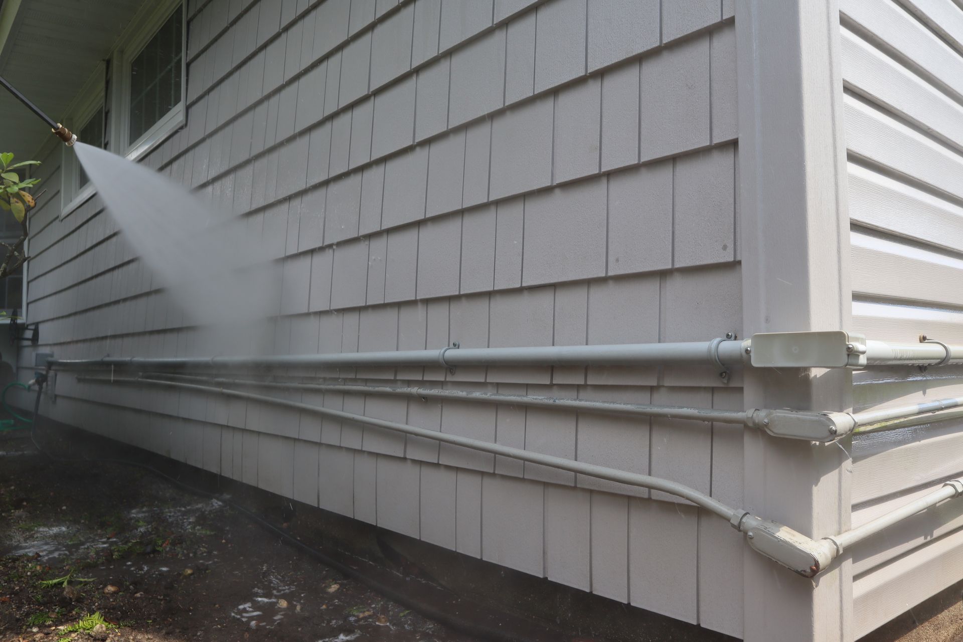 A person is using a pressure washer to clean the side of a house