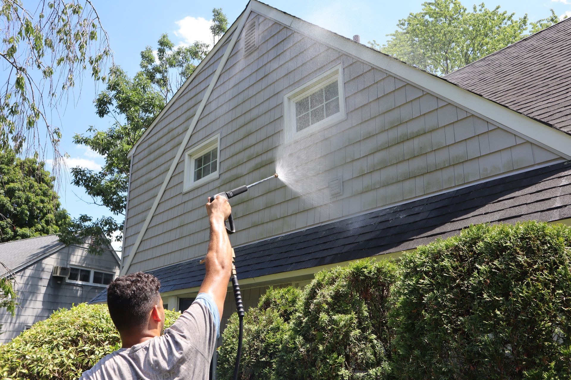 A man is using a pressure washer to clean the side of a house